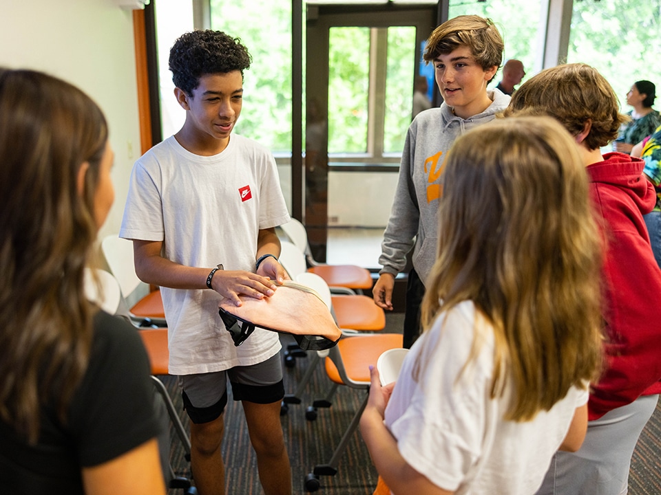 A Bearden Middle School student holds an orange fanny pack out while talking to four other middle school students circled around him.