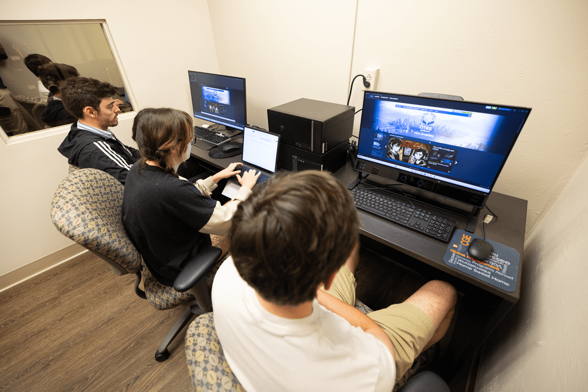 Three students sit in the user experience lab in front of two computer monitors while conducting testing.