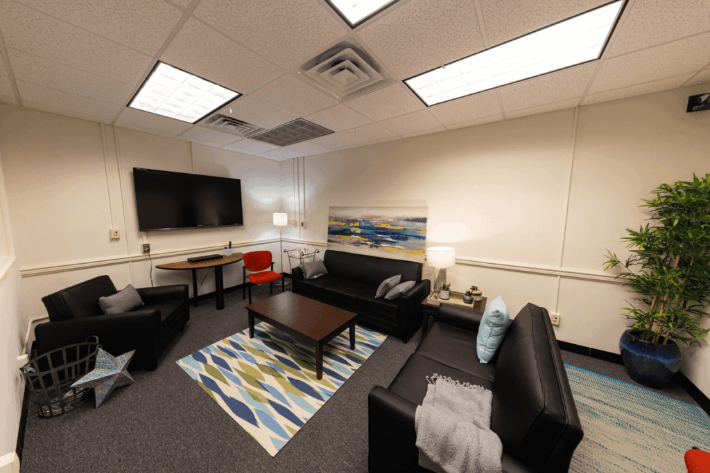 The Message Effects Lab has a living room set up with three couches around a coffee table with a rug under it, and a television screen mounted higher on the wall.