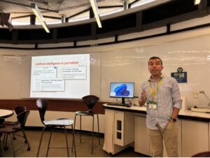 Assistant Professor Mustafa Oz stands in the foreground to the right with desks and a projected screen in the background to the right.
