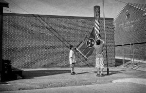 A black and white photo shows children lowering a Tennessee and American flag from a flagpole