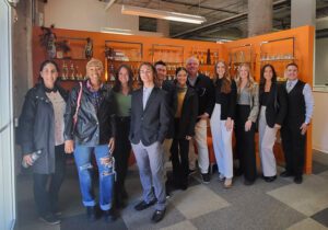 A group of advertising and public relations faculty and students stand before an orange background.