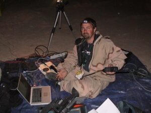 Jerry Simonson sits on a tarp with a laptop and camera equipment while covering the first war in Iraq.