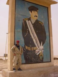 Jerry Simonson posing with a large mural of Sadam Hussein in Iraq.