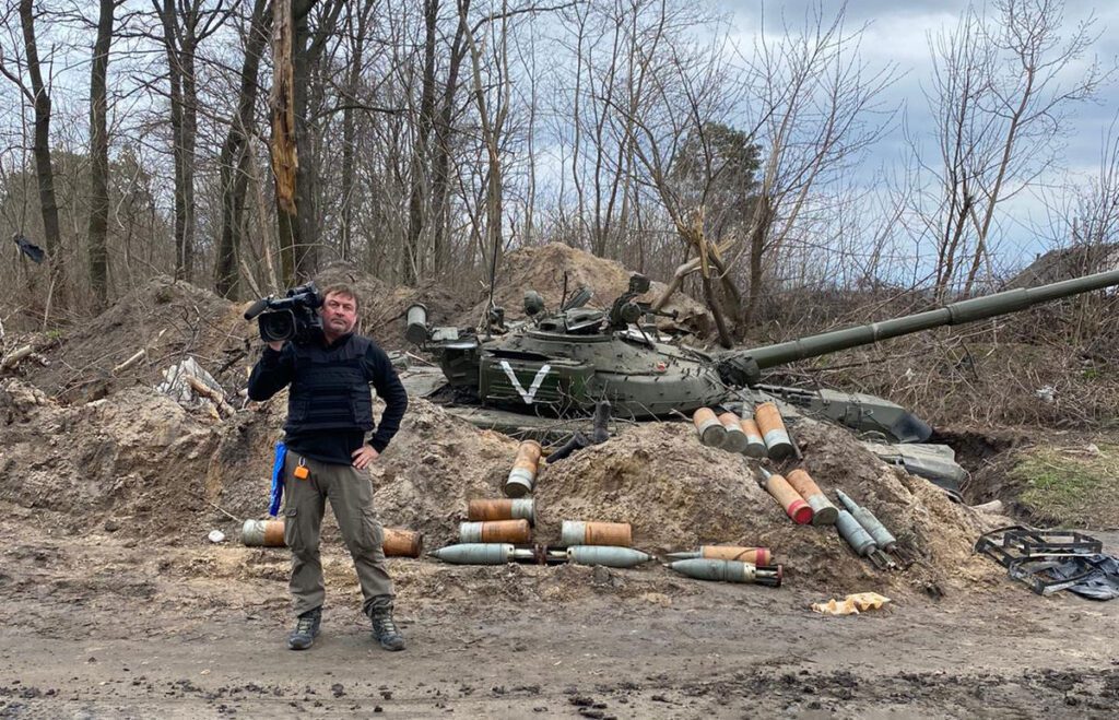 Jerry Simonson, JEM alum, with his camera equipment standing in rubble in Ukraine.
