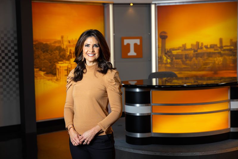 Former WBIR-TV news anchor Beth Haynes poses in the student broadcasting studio, which has an orange skyline of Knoxville and a Power T behind her.