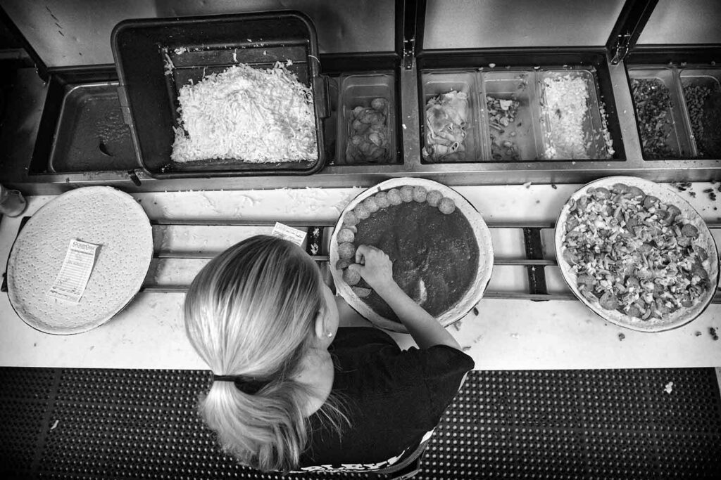 A black and white photo from a top down view shows a woman making pizzas.