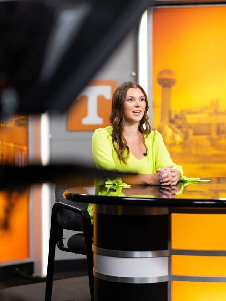 A Journalism and Electronic Media student sits at the anchor desk in the The Volunteer Channel studio.