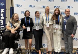 Five students are in front of a PRSA backdrop with Assistant Professor of Practice Joe Stabb.