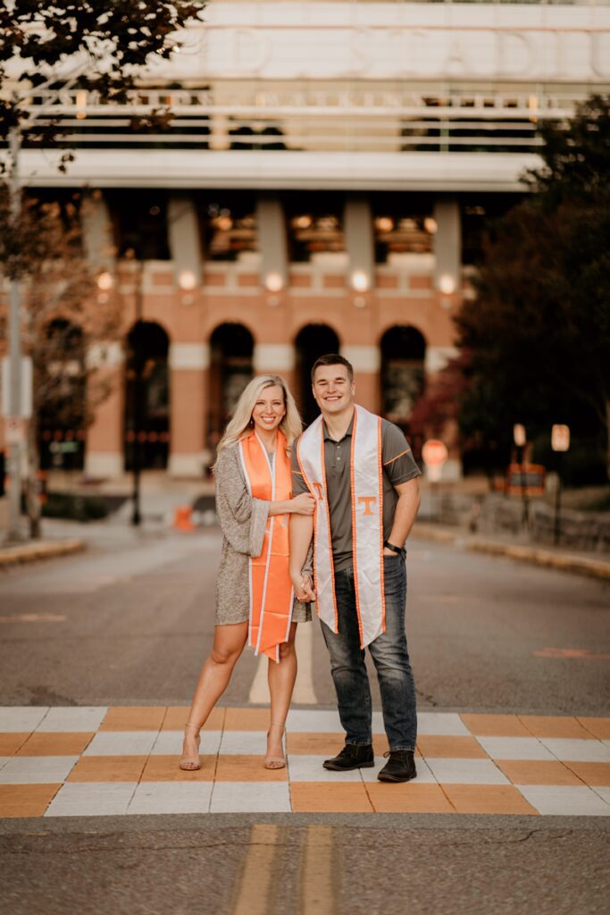 Kaitlin Shayotovich poses in front of Neyland Stadium with her husband, both wearing UT graduation garb.