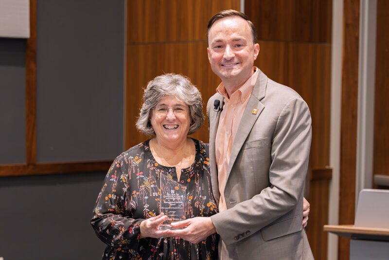 Clinical Professor Cindy Welch stands left of Dean Joe Mazer, both smiling broadly as she holds an award signifying her 15 years of working at the School of Information Sciences