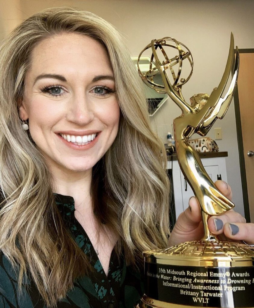 A smiling Brittany Tarwater holds a gold and black award depicting a winged woman holding a globe.