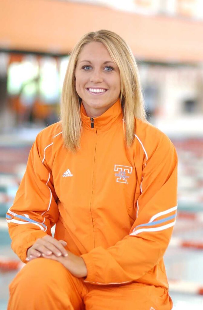 Brittany Tarwater is decked out in an orange and white track suit and sits in front of a lane swimming pool. 