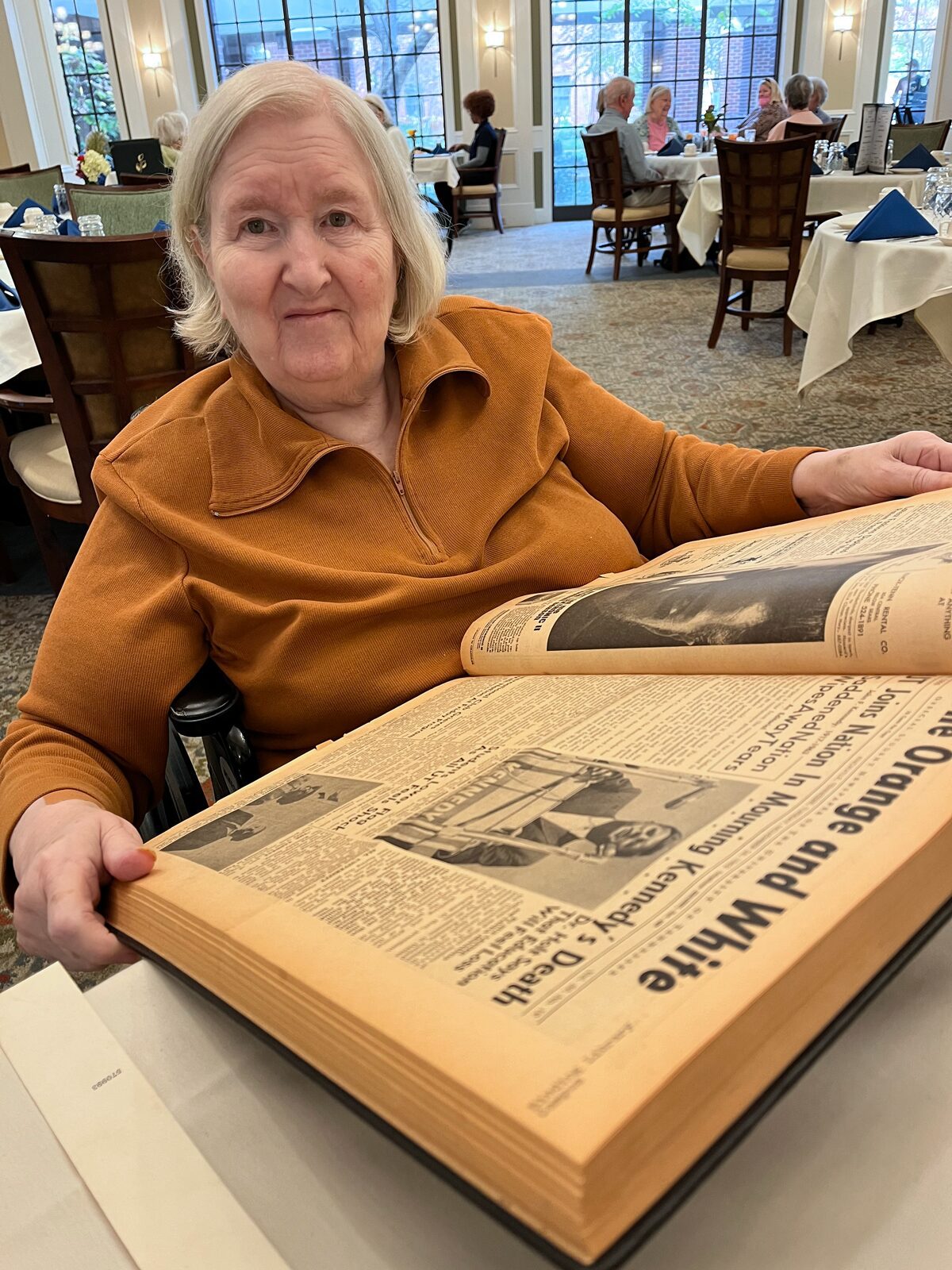 Linda Higgins wears an orange shirt as she sits at a desk and looks at archival copies of the Orange and White editions she helmed.