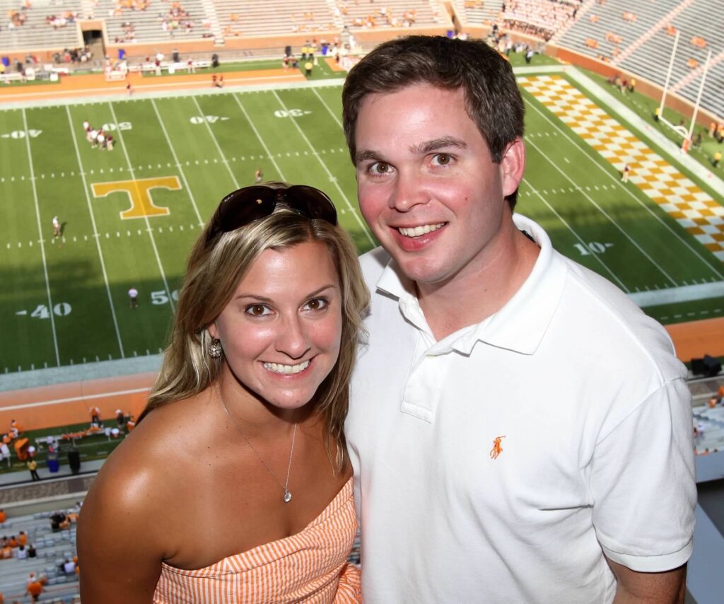 A young Erin and Lee Freeman pose in Neyland Stadium bleachers with the football field behind them.
