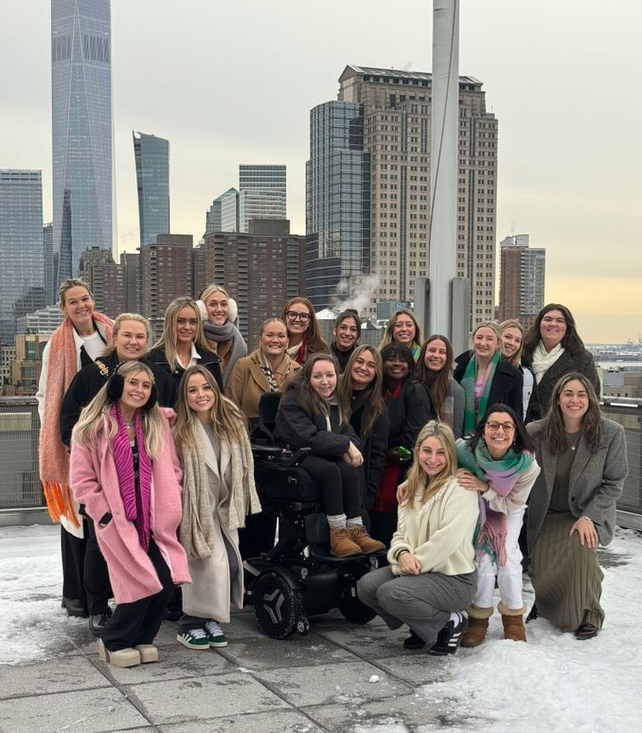 A group of ADPR and JEM students pose on top of a building with the New York City skyline behind them and snow all around on the ground.