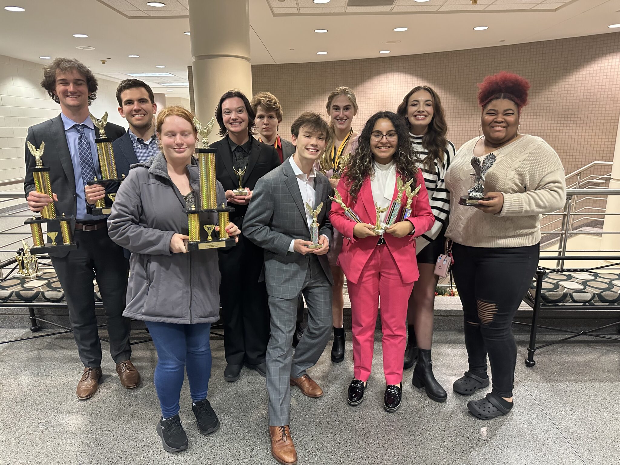 Eight members of the Tennessee Speech and Debate Society and their director, Abigail Barnes, pose for a group photo and hold up several trophies they have won.