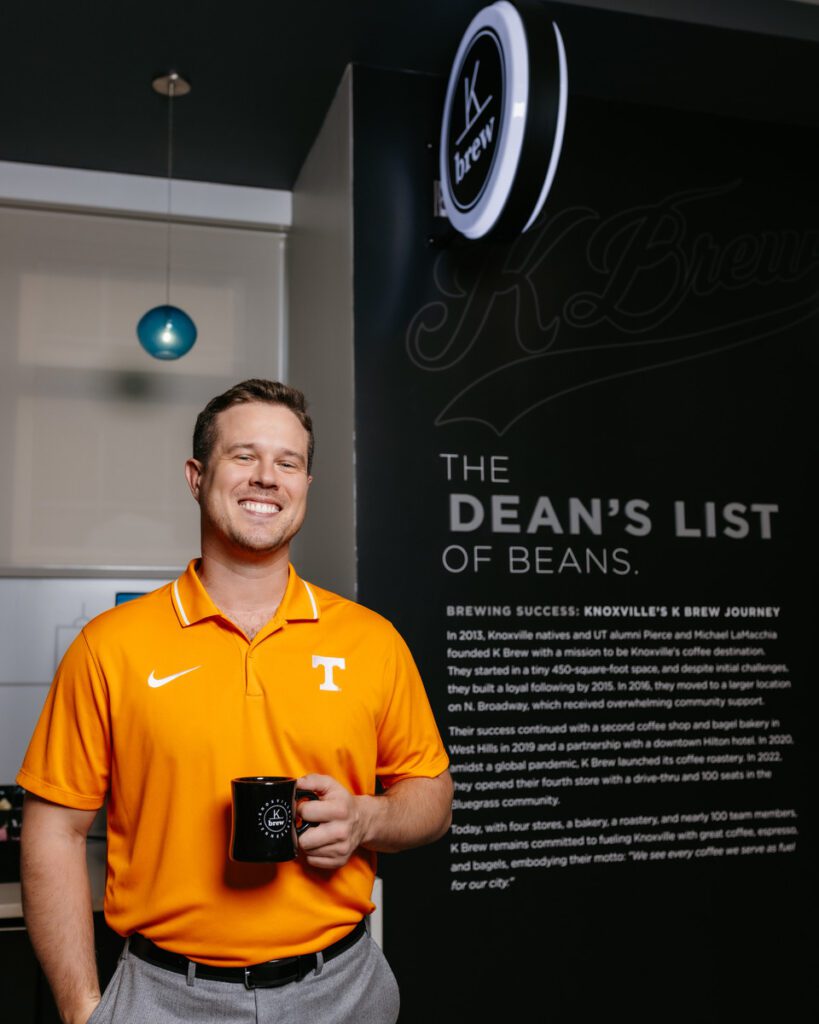 Pierce LaMacchia in front of the Dean's List of Beans sign holding a cup of coffee