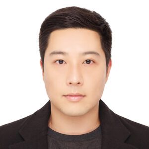 A headshot of Kibum young with a white background and he is wearing a black t-shirt with a black blazer.