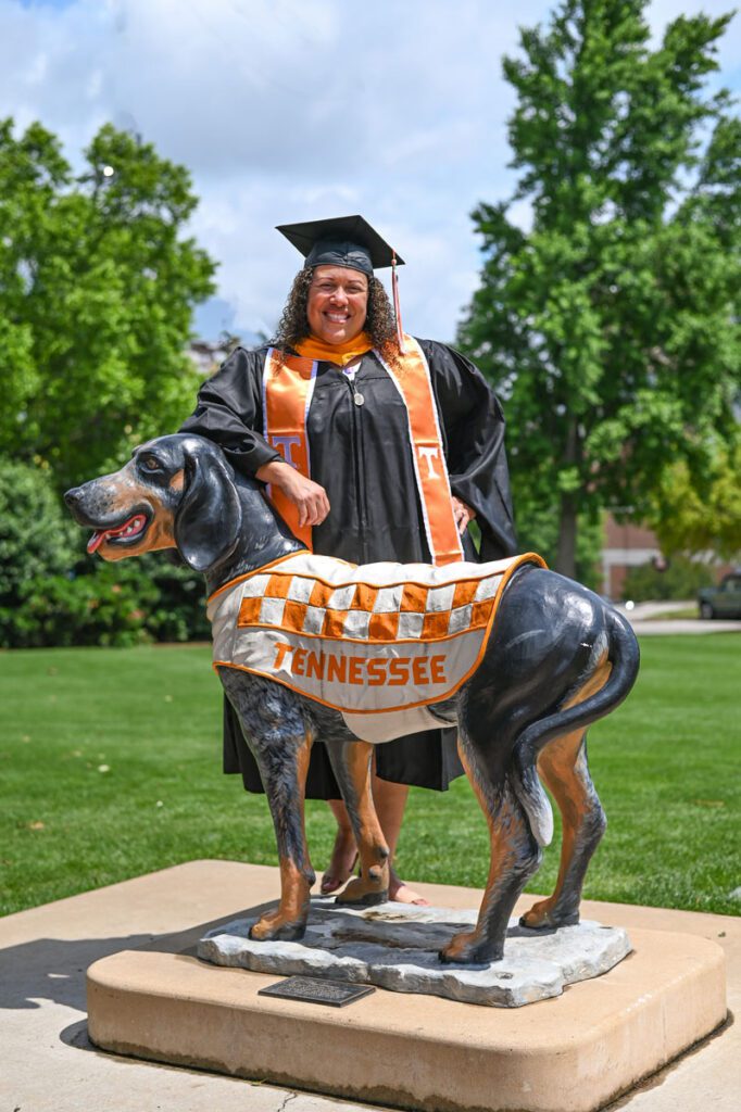Melissa Espinales wears her University of Tennessee, Knoxville, master's regalia for the Graduate Hooding Ceremony. She is standing behind one of the Smokey statues in Circle Park.
