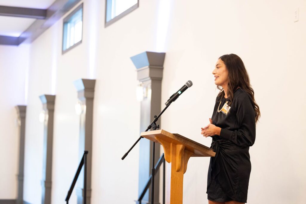 Abbey Barnes stands at a podium, wearing all black.