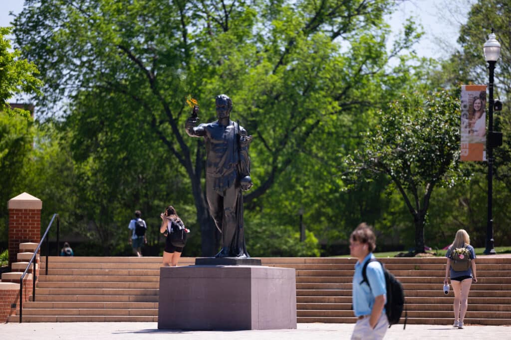 Students with backpacks on walk by the Torchbearer in Circle Park.