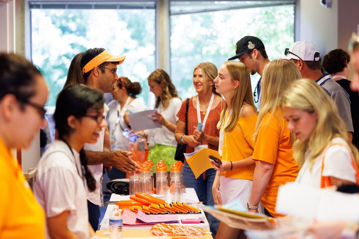 Several new students stand on the other side of a table across from CCI faculty and staff at a summer event.