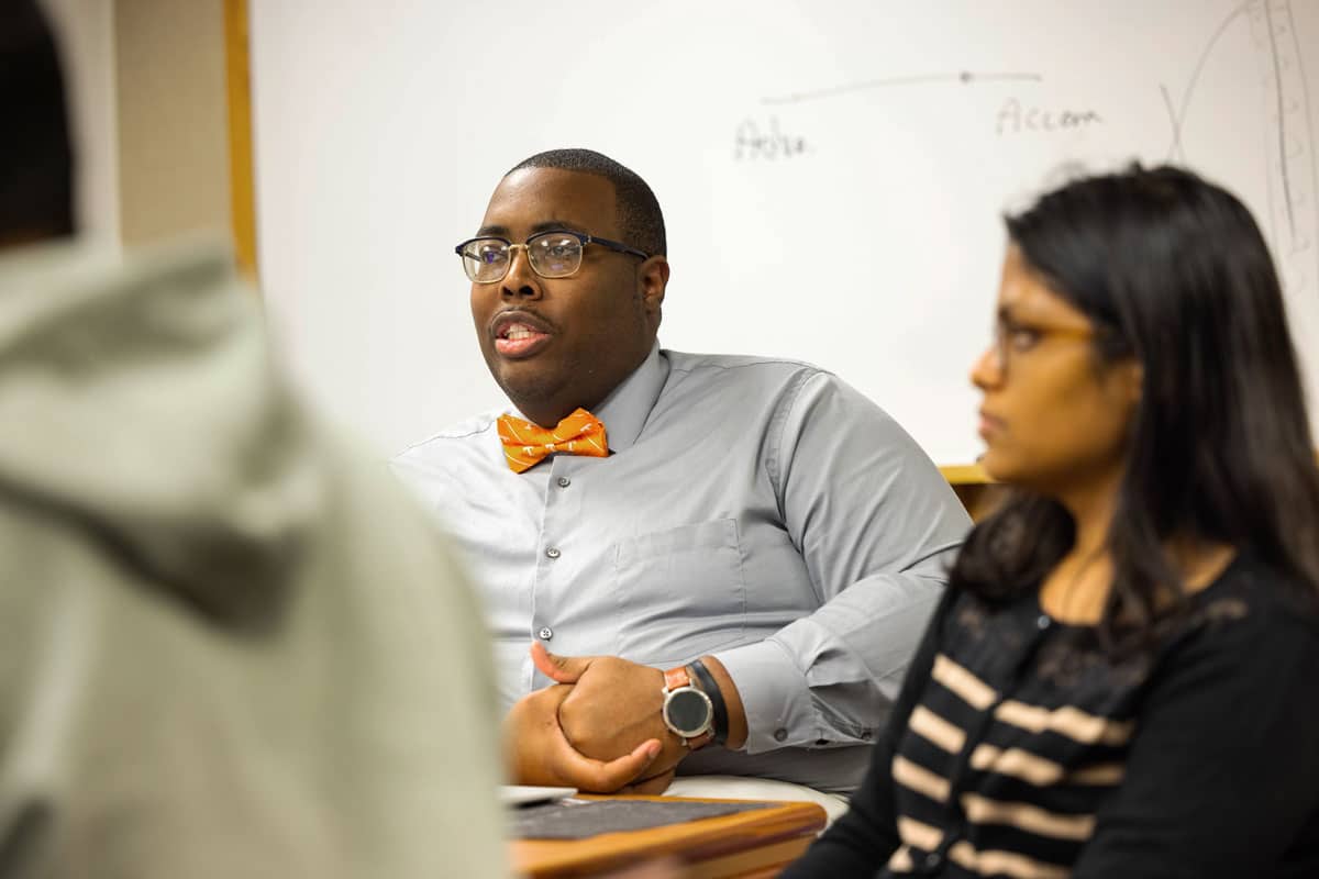 PhD student Byron Keyes speaks during a class; he's wearing a gray shirt and a Tennessee orange bowtie.