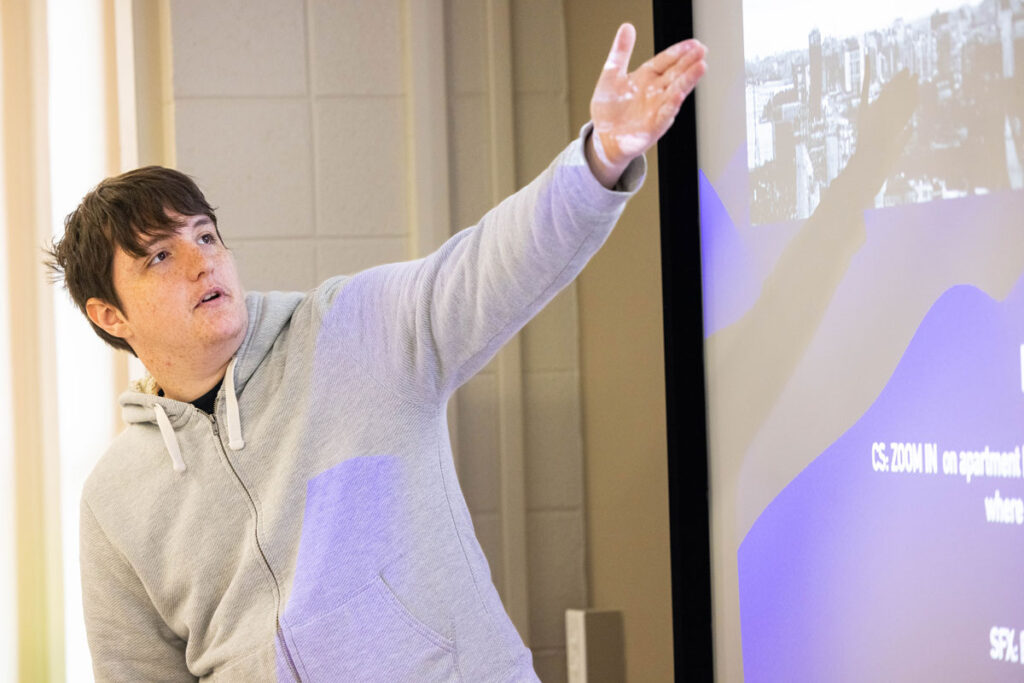 A student gestures to a presentation on a large screen in a class.