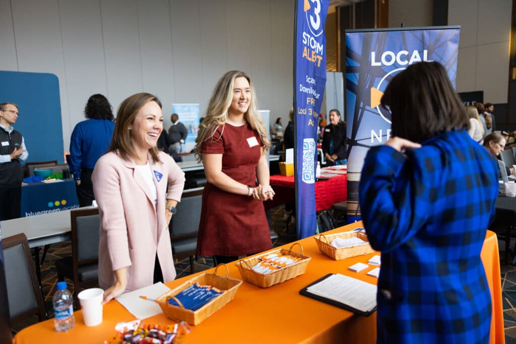 Two employees from an employer smile while talking to a student at a UT career fair.