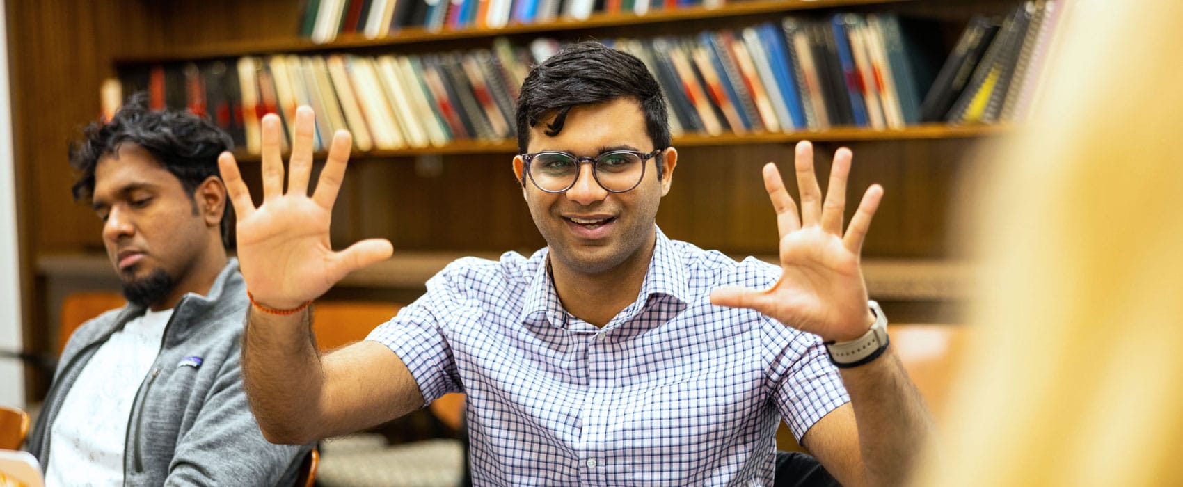 Aman Misra, a PhD student, holds both of his hands up with his fingers spread out as he smiles and speaks during a class.