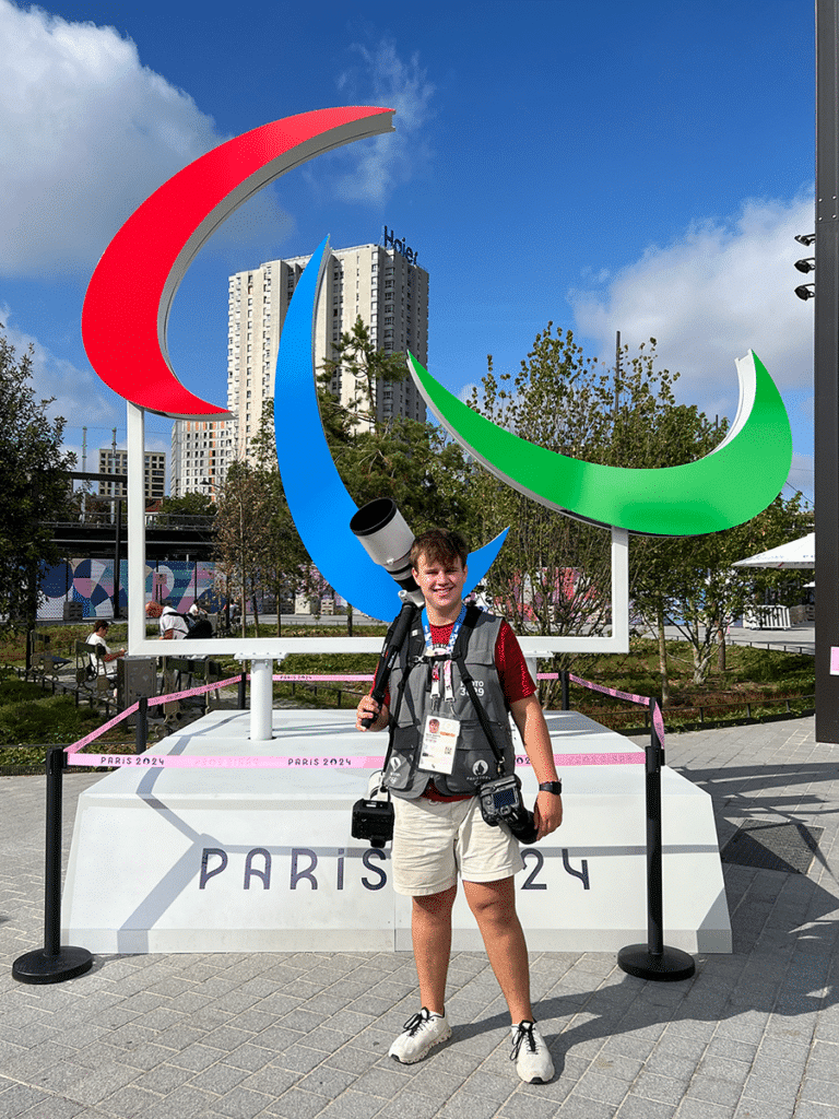 Sophomore Ryan Beatty poses with his camera equipment in front of a Paralympics statute at the Games in Paris.