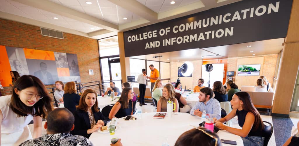 Several PhD and master's students studying communication or information sciences sit at tables in the college's lobby for a welcome lunch in their honor.
