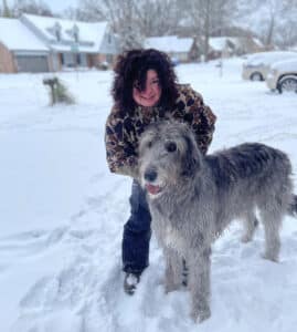 Teresa O'Daniel stands on a snow-covered street with a large Irish wolfhound