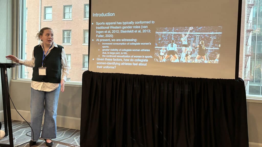 A photo of Helene Burch standing in front of a presentation slide as she talks about her research at the IACS summit in Chicago.