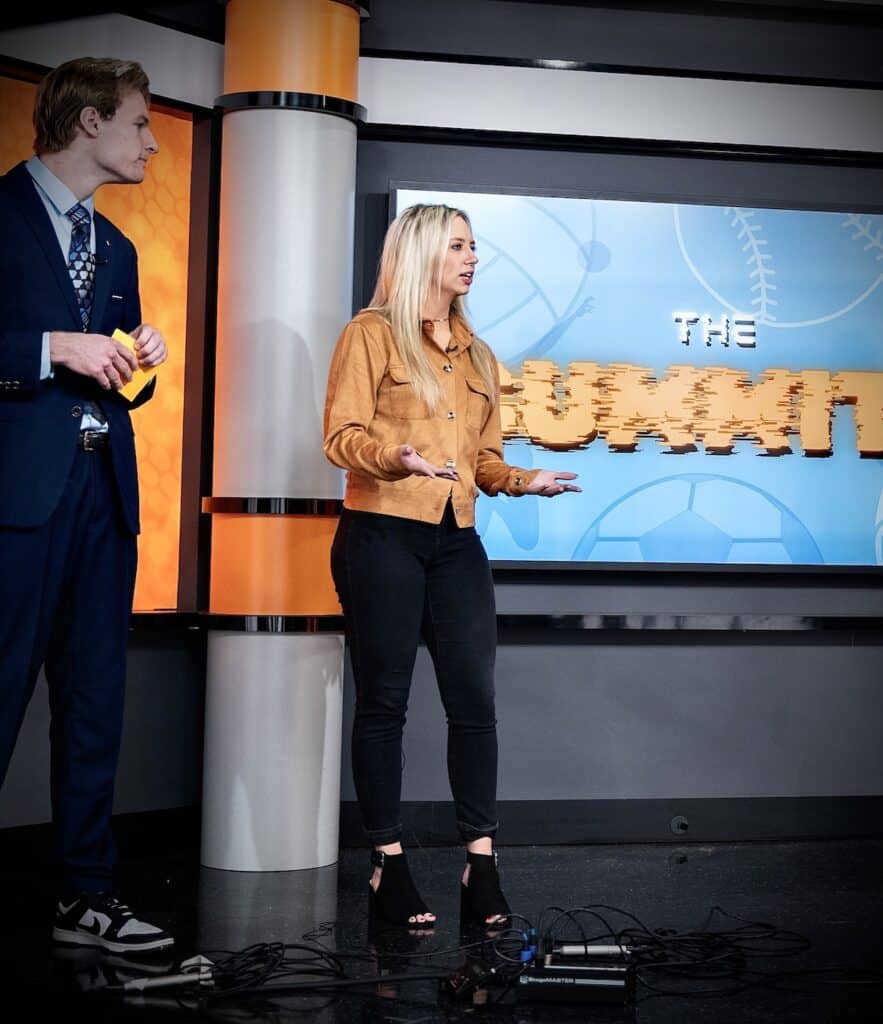 Alexie Cowan presenting in the TVC News studio in front of a tv screen that reads the summit