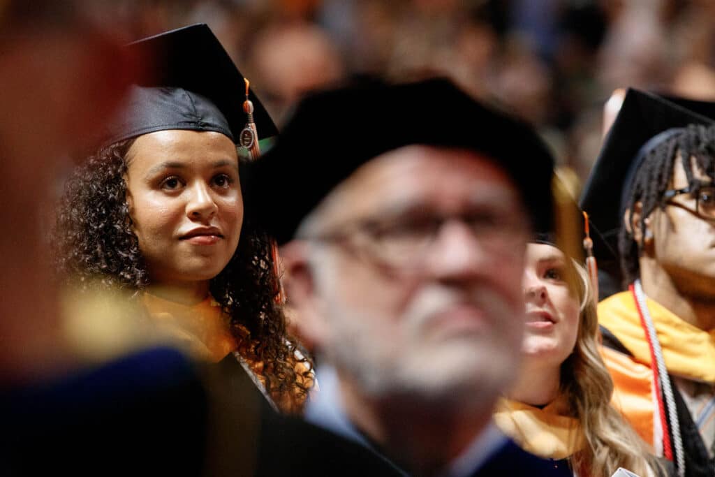 Riley West is in focus with faculty ad other students around her out of focus in the foreground at commencement.