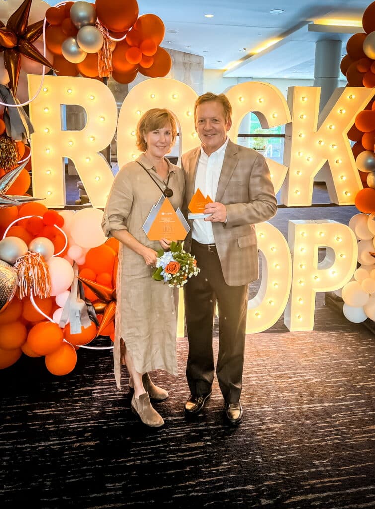 A photo of Sharon Oldham and Mark Oldham, co-founders of Oldham Hospitality, holding their first Rocky Top Business Award in front of a light up Rocky Top sign at the 2023 awards celebration.