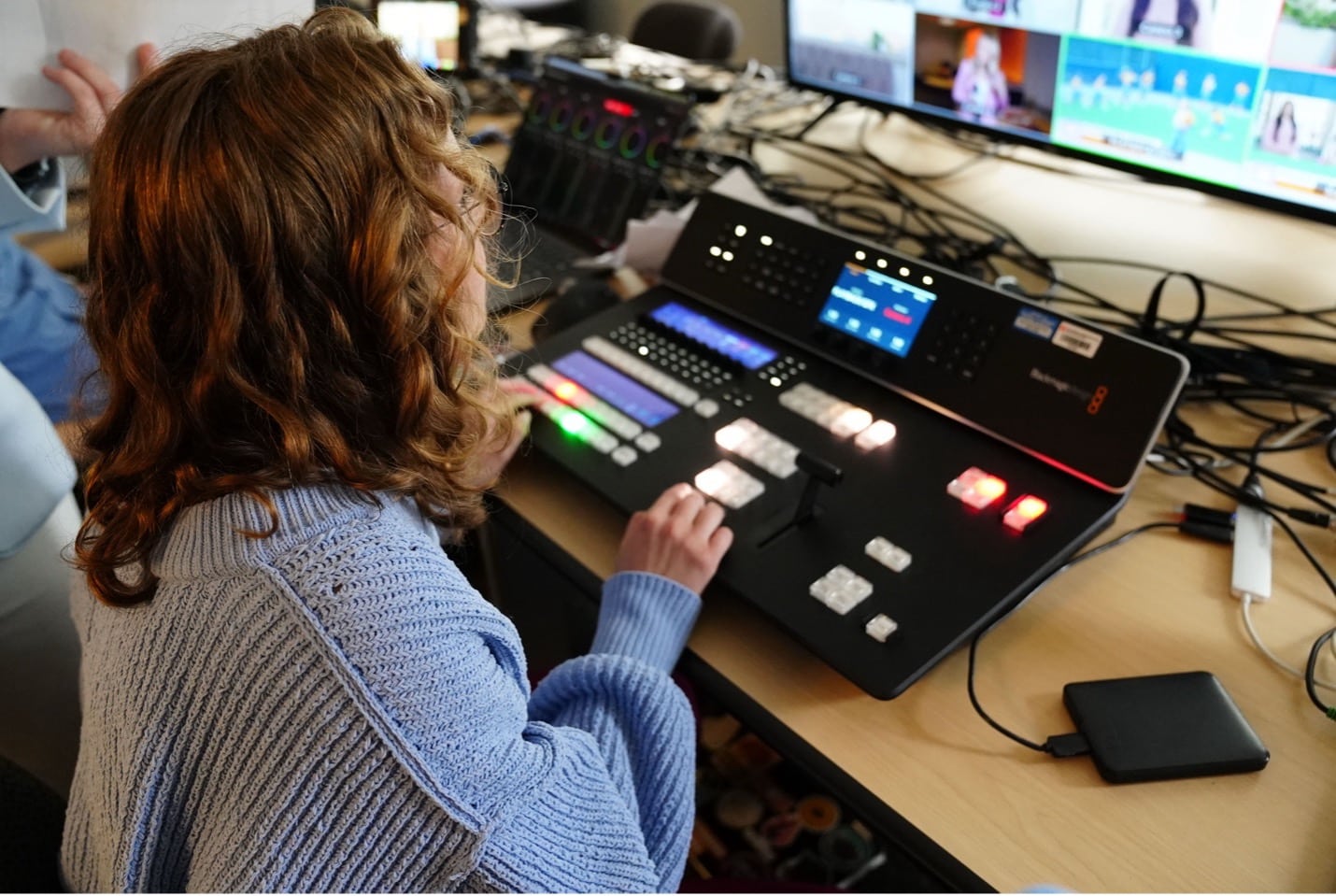 A student sits at a sound board while looking at a screen display.