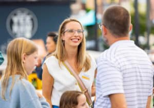 Jenny Crowley is at Yee-Haw Brewing during the National Communication Association's Doctoral Honors Seminar in summer 2025. She is smiling at a man whose back is to the camera, and there are two children to the left of the photo.