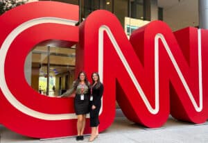 Students Gracyn Thatcher and Emma Browning stand in front of the large C-N-N sculpture logo.