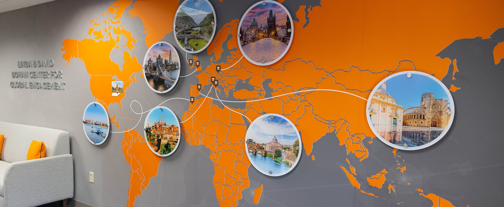 A wall installation features silver letters stating Linda and David Bohan Center for Global Engagement to the left, with a large U-T orange map on a dark grey wall and several circular photos of cities placed where C-C-I takes students for study abroad trips.