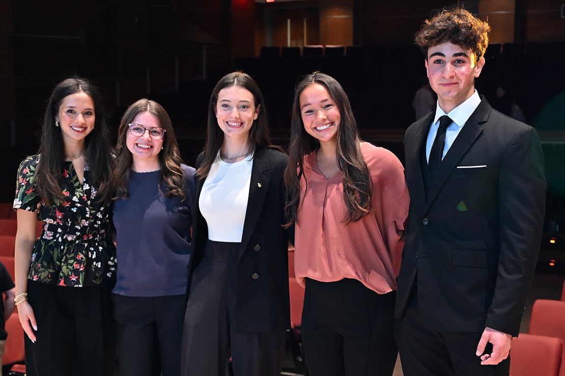 Five students in business professional pose in an auditorium.