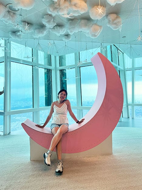 Samantha Ho sitting on a pink crescent moon sculpture