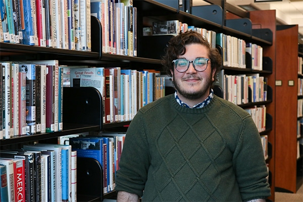 An alum of the information sciences master's program stands in front of a library stack.