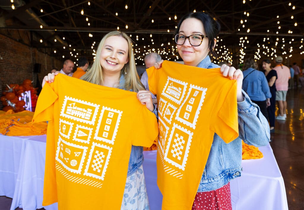 Two C-C-I employees hold up U-T orange shirts with a white design on them, smiling.
